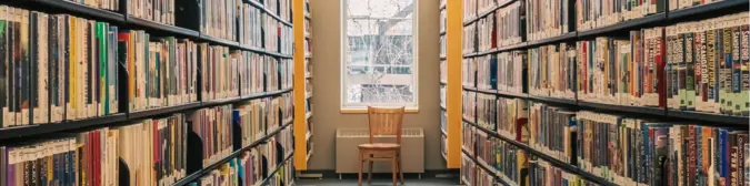 A wooden chair at the end of two book aisles.